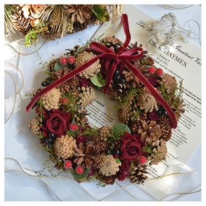 Detail of Christmas wreath with red roses, natural pine cones and a velvet bow