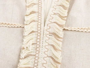 Détail macro de franges à glands et bordure tissée en fil d'or sur robe en lin