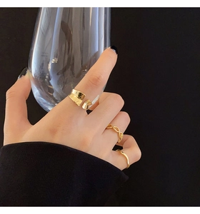 Close-up of three layered gold-plated rings including a twisted band and open wide ring