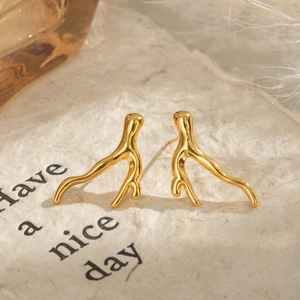 Boucles d'oreilles branche minimalistes dorées sur papier texturé avec lumière naturelle