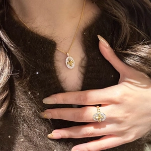 Detailed view of 18k gold plated oval Fleur-de-lis ring and necklace set on a model