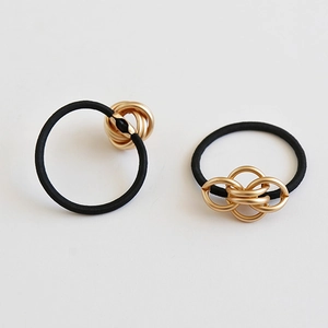 Minimalist black elastic hair tie with interlocking gold metal knots on a white background