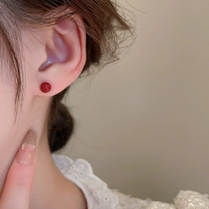 Close-up of red spherical stud earrings with gold plating worn on model's ear
