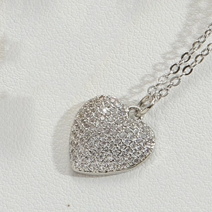 Macro shot of silver heart pendant necklace with shimmering paved crystals on white leather