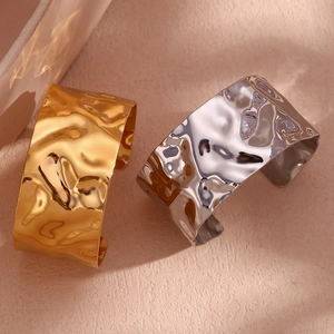 Detail of wide open metal bangles with hammered lava texture in gold and silver finish