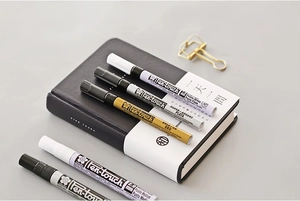 Detail of Sakura Pen-touch markers in gold, silver, and white on a black notebook
