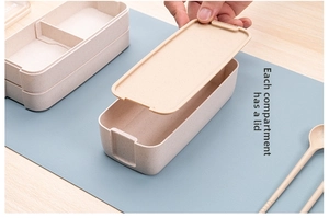 Close-up of double-layer microwave safe lunch box with lid and utensils on blue placemat