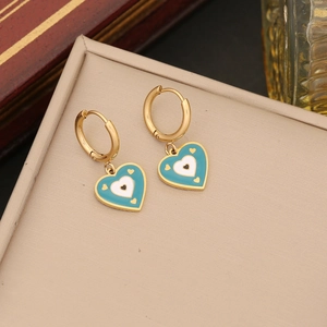 Bohemian gold heart earrings with blue enamel eye charm on a beige jewelry case
