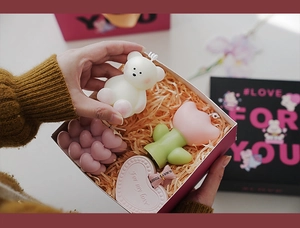 Detailed view of hand opening a gift box with bear and floral scented candles