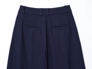 Detail of navy blue pleated trousers showing belt loops and dual rear welt pockets
