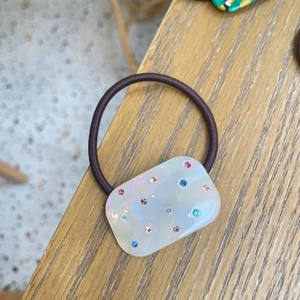 Brown elastic hair tie with pearl-white rectangular acrylic piece and colorful rhinestones