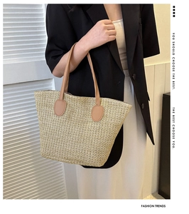 Detail of a woven straw tote bag with brown leather handles and spacious design