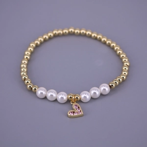 Detail of gold beaded bracelet featuring white pearls and a pink zircon heart charm