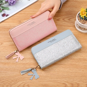 Detail of long sequin wallets with fringe zipper and bow charm on a wooden surface