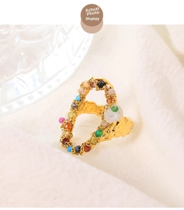 Detailed side view of a heart-shaped golden ring with colorful beads on white cloth