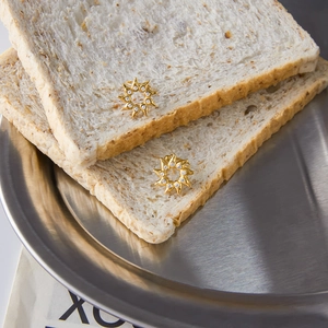 Detailed view of golden sun-shaped zircon earrings placed on rustic bread background