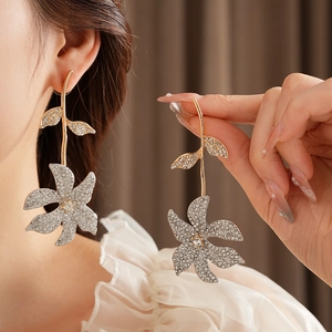 Detailed view of large gold flower earrings with silver rhinestones on model's ear