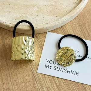 Detail of gold metal hair ties with hammered texture on a rustic stone tray background