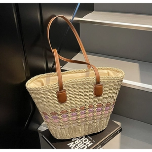 Close-up of beige woven straw tote bag with pink floral patterns and leather straps