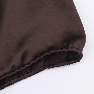 Dettaglio della manica di una camicia in raso marrone scuro con polsino elasticizzato