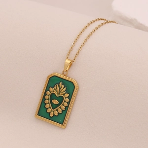 Collier tarot coeur en acier doré avec pendentif émail vert sur fond beige texturé