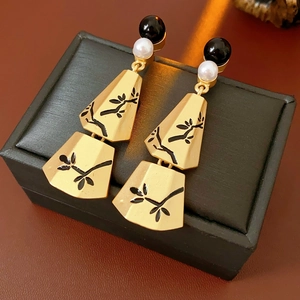 Detail of golden geometric earrings with black branch pattern and pearls on jewelry box
