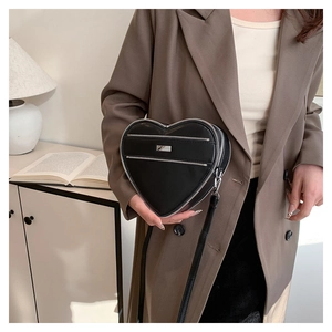 Detail of a chic heart-shaped black crossbody bag with silver zippers and metal hardware