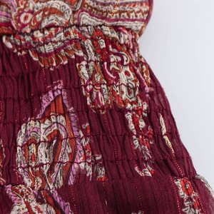 Détail macro du tissu paisley rouge foncé avec fils dorés et texture smockée extensible