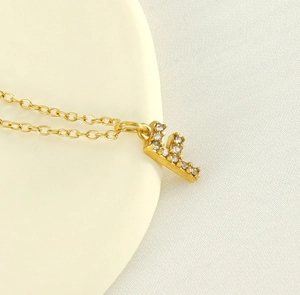 Macro shot of gold letter E necklace pendant with sparkling zircon inlays on fabric