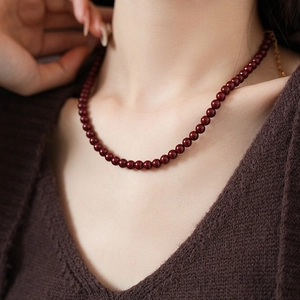 Detail of dark red beaded titanium steel necklace on model with polished finish