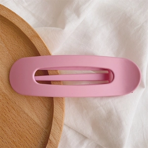 Close-up of a matte pink hollow oval duckbill hair clip on a minimalist wooden tray
