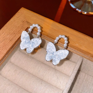 Macro shot of blue crystal butterfly earrings with pearl details on wooden tray