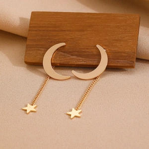 Detailed view of golden moon and star tassel earrings resting on dark wood background