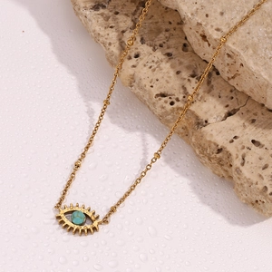 Close-up of 18K gold-plated evil eye necklace with turquoise stone on a beige rock