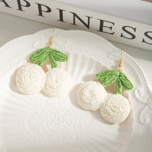 Detail of handmade bohemian white cherry earrings with green leaves on ceramic plate