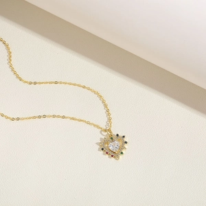 Macro detail of heart pendant with central white zircon and colorful stones on gold chain