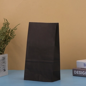 Detailed view of a plain black kraft paper gift bag on a clean minimalist studio setup