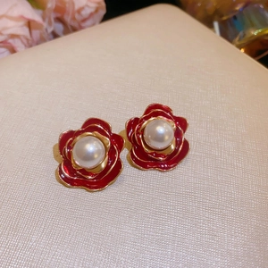 Nahaufnahme von roten Rosenohrringen mit Perle und elegantem goldenem Metallrand