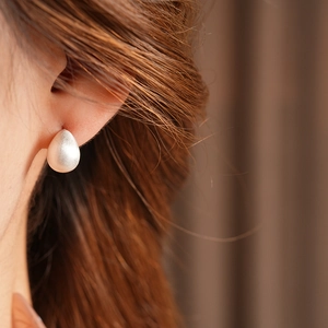 Macro shot of matte white teardrop earring on model showing minimalist brushed texture
