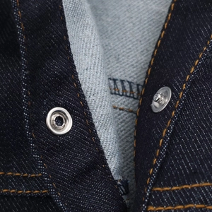 Detailed close-up of dark blue denim fabric with silver metal buttons and orange stitching
