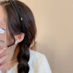 Détail d'un serre-tête noir en tissu avec logo doré et boucle d'oreille en perle élégante