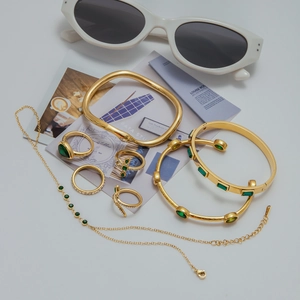 Flat lay of gold stainless steel jewelry set featuring emerald green gemstones and bracelets