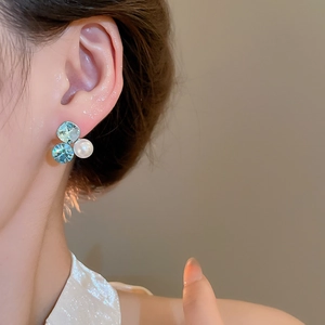 Macro shot of 18k gold plated earrings featuring green zircon and round white pearl details