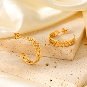 Close-up of golden C-shaped hoop earrings with intricate hollow woven texture on stone