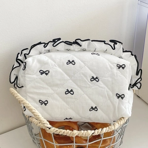 Detail of quilted makeup bag with bow embroidery and ruffled edges in a woven basket