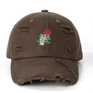 Close-up of skeleton hand holding red rose embroidery on brown distressed baseball cap