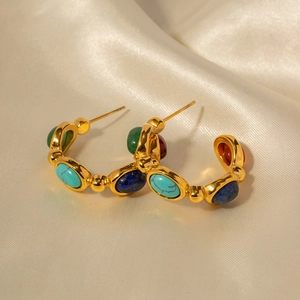Detailed close-up of 18K gold plated C-shaped earrings with colorful oval stones on silk