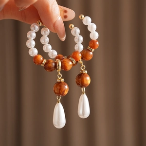 Detail view of water drop pearl earrings with amber beads held against a soft background