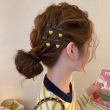 Detail of two mini dark hair clips with yellow heart accents worn on a braided hairstyle