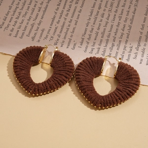Detail of heart-shaped earrings with brown woven yarn texture and golden metallic accents